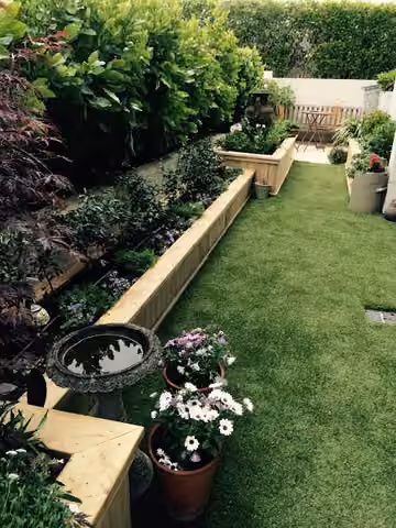 Artificial lawn beside planted garden beds and flower pots